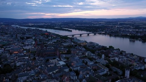 High Drone aerial shot of Mainz at magic hour night circling around city center with with the cathedral and the dark Rhine river water in the background showing a colorful sky