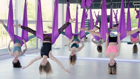 Group of young women practice in aero stretching swing. Aerial flying yoga exercises practice in purple hammock in fitness club. 28may2021 St.Petersburg Russia.