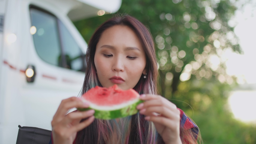 Portrait of an asian female in nature, a young woman eating a watermelon and enjoying fruit food, summertime, picnic in nature.