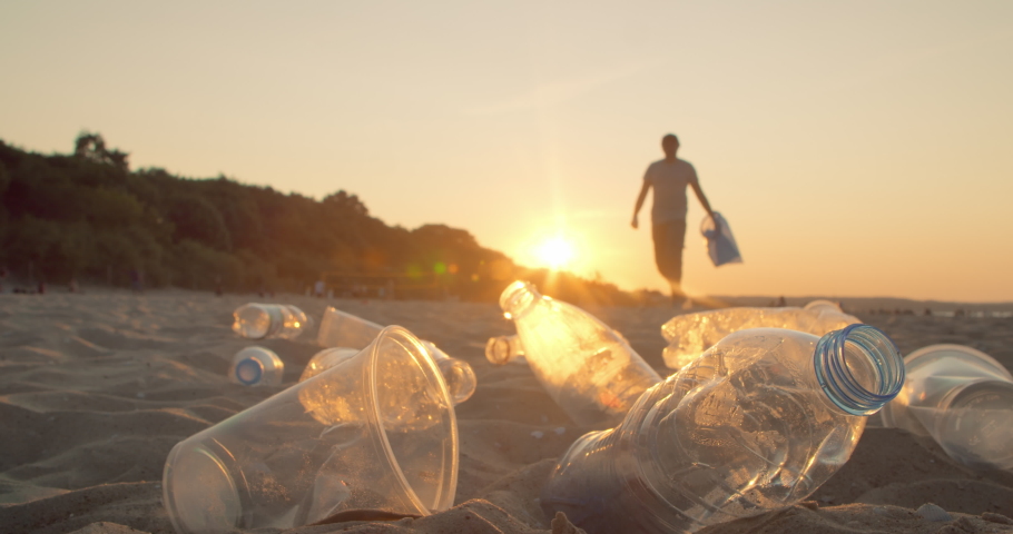 Volunteer with a bag in his hand cleans the beach from plastic garbage. Concept of waste environment, recycle, ecology, pollution and volunteer.  Royalty-Free Stock Footage #1075869158