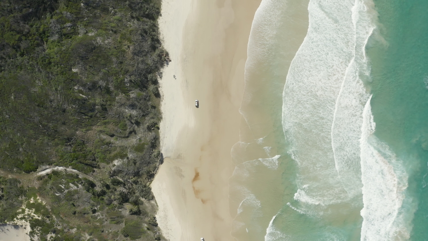 4k drone top view of a car driving along the beautiful beach on Fraser Island, Australia.