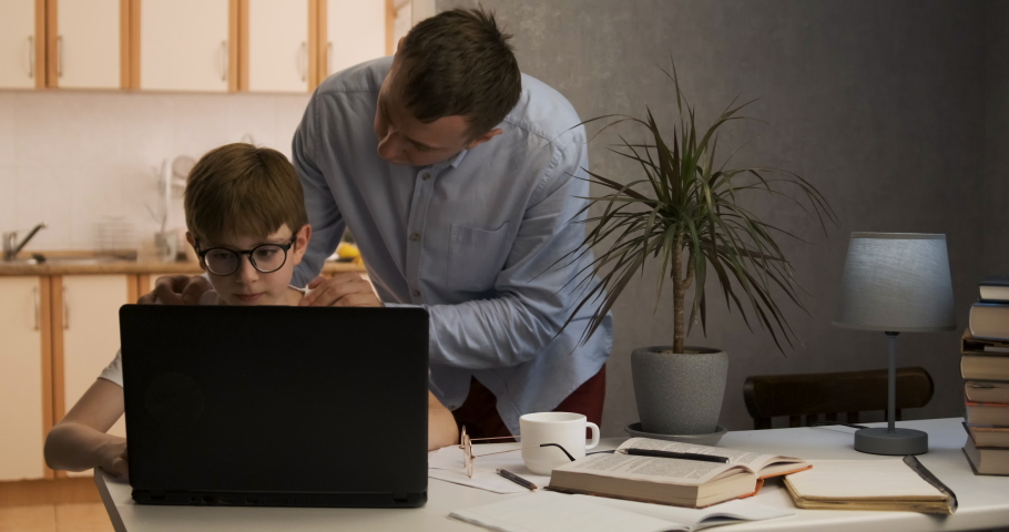 Boy sits at laptop while his father cheers him on. Father supports his son in his endeavors. Royalty-Free Stock Footage #1075871483