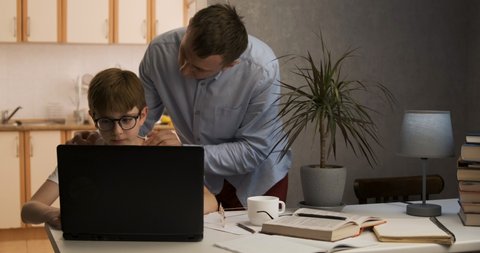 Boy sits at laptop while his father cheers him on. Father supports his son in his endeavors.