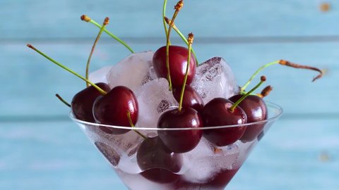 Close up cherries in ice cubes covered with refreshing drops of water in a martini glass on a blue wooden background
