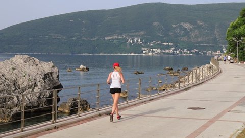 Beautiful blonde jogging early in the morning in Kotor Bay, Montenegro. People go in for sports, walk. A child rides electric scooter near a mountain landscape in Herceg Novi, Montenegro, 2021-06-22