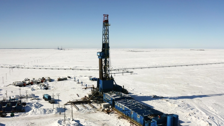 A large drilling rig stands in the center of the ice field. Oil and gas production is underway. Technical buildings can be seen around the drilling rig. Royalty-Free Stock Footage #1075875728