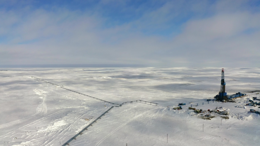 A large drilling rig stands in the center of the ice field. Oil and gas production is underway. Technical buildings can be seen around the drilling rig. Royalty-Free Stock Footage #1075875731