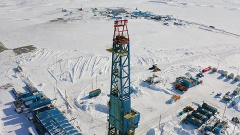 A large drilling rig stands in the center of the ice field. Oil and gas production is underway. Technical buildings can be seen around the drilling rig.