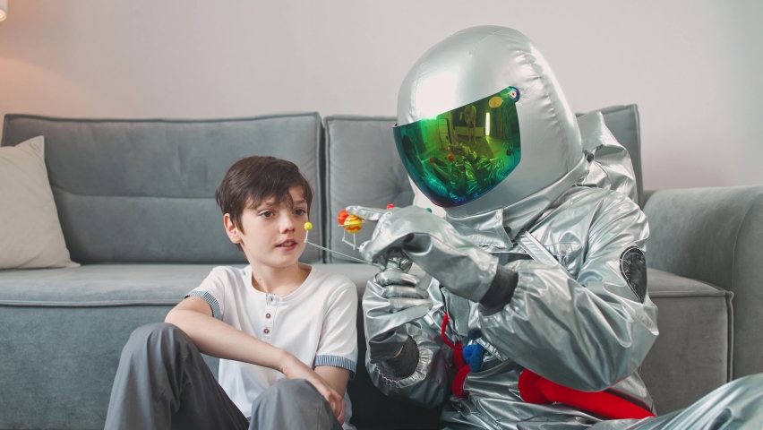 Father and son play in the living room at home, father in an astronaut costume sitting on the floor with her son, boy playing with a toy model of the solar system, study of astronomy, 4k slow motion.