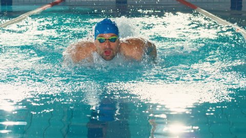 Successful Male Swimmer Racing, Swimming in Swimming Pool. Professional Athlete Determined to Win Championship using Butterfly Style. Colorful Artistic Cinematic Style. Front View Tracking Shot