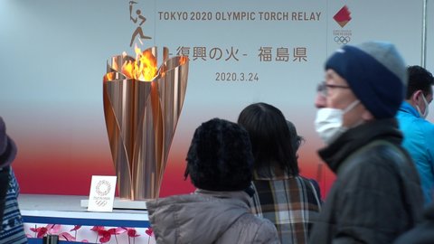 FUKUSHIMA, JAPAN - 24 MARCH 2020 : Olympic Flame displayed at Fukushima station. Tokyo Olympic 2020 have been postponed to 2021 due to coronavirus. Crowd of people wearing surgical masks.