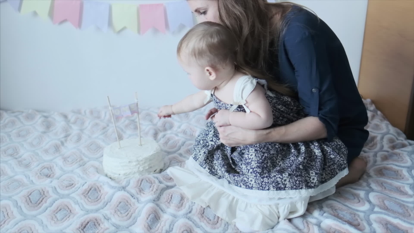 Mother shows the first birthday cake to her daughter with candle on it during celebration at home