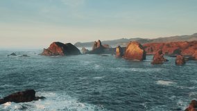 Scenic shore landscape view with cinematic flat narrow sea rocks in bright orange sunlight at sunset. USA, beautiful aerial footage Gold Beach cliffs, Oregon coast, Rocks on west coast, Pacific Ocean