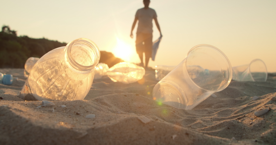 Cleaning the beach from plastic garbage. Volunteer picks up plastic garbage and throws a plastic bottle into the bag. The concept of volunteering and waste recycling. | Shutterstock HD Video #1075887101