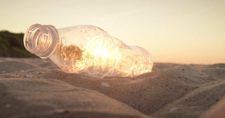Cleaning the beach from plastic garbage. Close-up, a volunteer hand picks up a plastic bottle from a sandy beach and throws it into a bag at sunset. The concept of volunteering and waste recycling.  Royalty-Free Stock Footage #1075887104