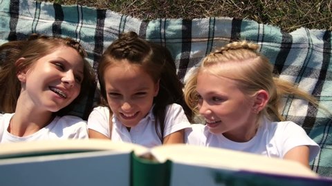Girls lie on the carpet in nature and read a book. Happy children relax in the camp. Schoolchildren in nature.