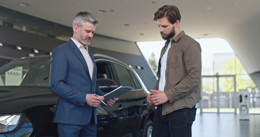 Bearded man is signing documents at car center. He is shaking hands with car dealer. Selling and business concept. | Shutterstock HD Video #1075896038