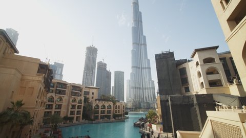 Tourist looking at urban city center of Dubai with Burj Khalifa skyscraper. Dolly out view of a woman on a balcony overlooking luxury tourist resort by the pool Dubai, UAE in 2021