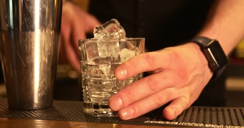 The bartender pours ice cubes into a cocktail glass. Bar.