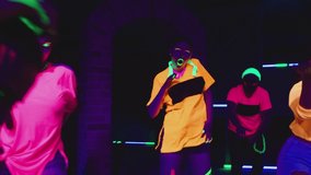 Group of female and male stylish dancers dancing inside dark place with neon lights .  Beautiful young people with fluorescent colorful make-up and clothes dancing in UV light. 4K video in slow motion