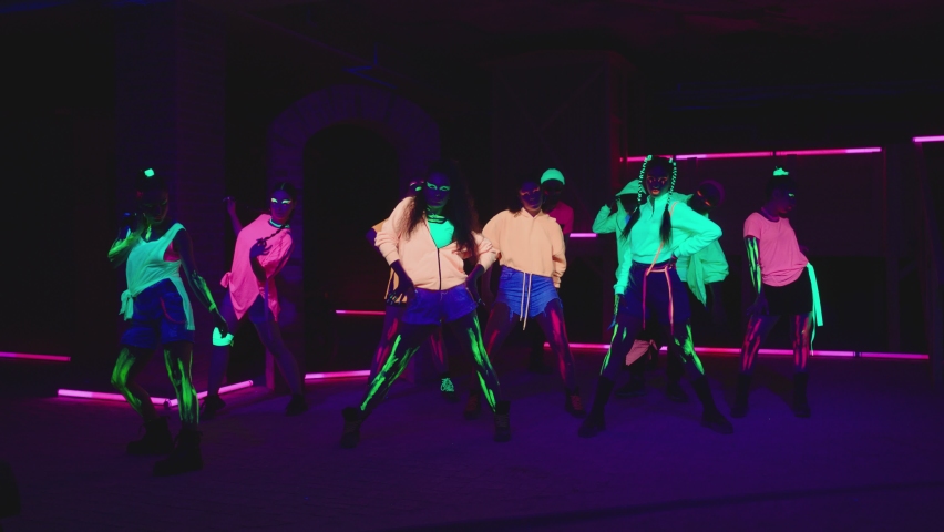 Group of female and male stylish dancers dancing inside dark place with neon lights .  Beautiful young people with fluorescent colorful make-up and clothes dancing in UV light. 4K video in slow motion