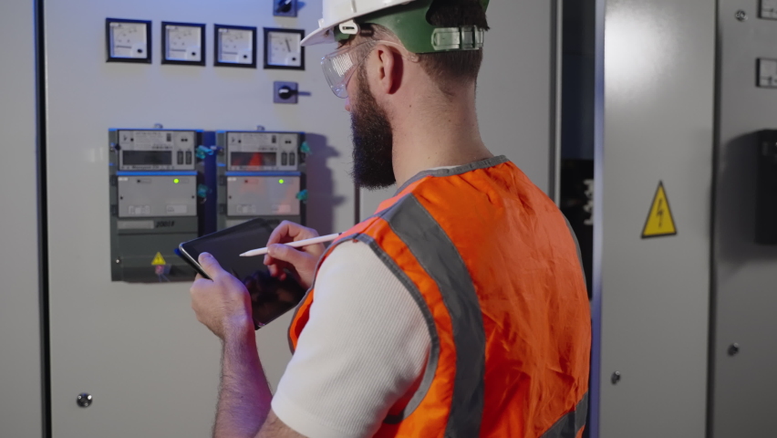 engineer is controlling metering on electric panel and filling report in tablet, worker of electrical engineering service is controlling electricity consumption Royalty-Free Stock Footage #1075903712