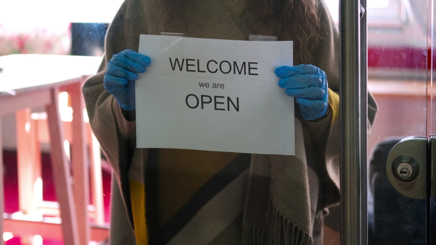 Owner of the storefront cafe in gloves attaching the announcement that cafe is open. Easing some requirements of COVID-19 prevention and protection Royalty-Free Stock Footage #1075903730