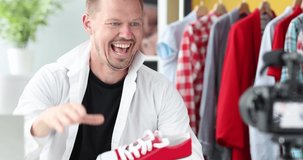 Enthusiastic male blogger demonstrates red sneakers to camera 4k movie