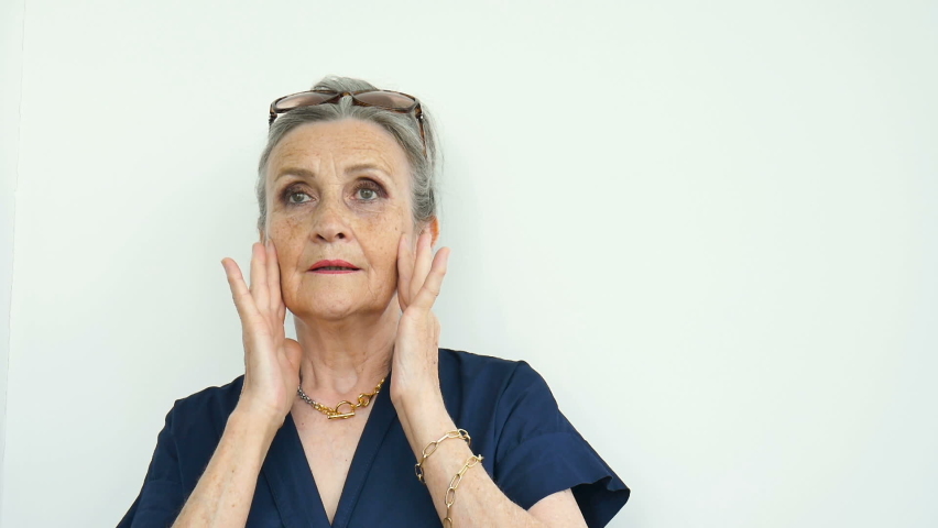 Indoors portrait of anxious shocked senior woman under shock with both hands on face due to fear and stress over white background, stressful retirement, bad news