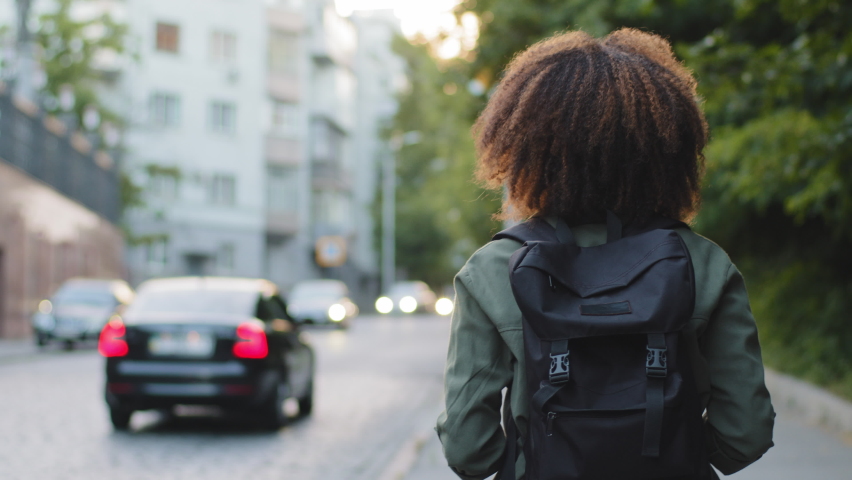 Curly-haired girl tourist with backpack walking along road photographing attractions in big city. Young woman photographer blogger sightseeing takes pictures using professional camera during travel