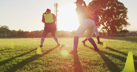 Diverse group of female baseball players exercising on pitch, running between cones. female baseball team, sports training and game tactics.