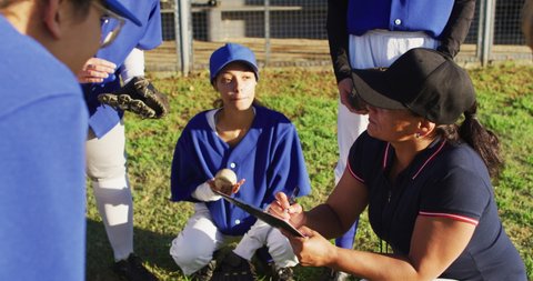 Diverse group of female baseball players listening to female coach, squatting and talking on pitch. female baseball team, sports training and game tactics.