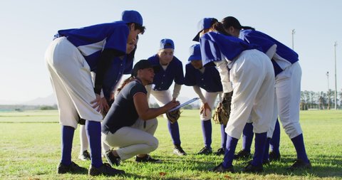 Diverse group of female baseball players huddled around female coach, squatting and talking on pitch. female baseball team, sports training and game tactics.
