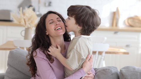 Funny kid kiss happy laughing mum greeting female parent with mother day or birthday. Young caucasian family together at home on weekend or lockdown spend time cuddling bonding. Love and tenderness