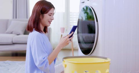 asian woman do the laundry in smart washing machine and use smartphone operate it at home
