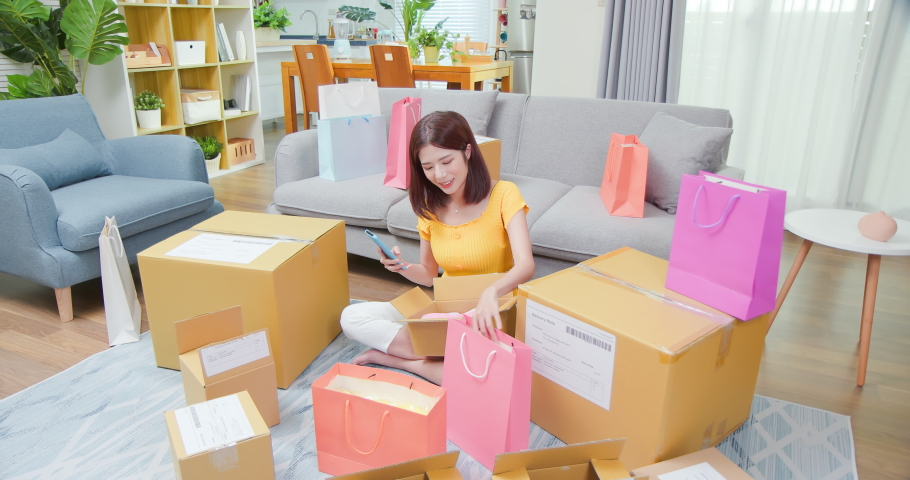 happy asian woman receive packing parcel after online shopping at home and she check order list on mobile phone in opening delivery boxes or bags Royalty-Free Stock Footage #1075922387