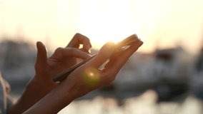 Close-up with the rays of the setting sun, a woman hands holding a smartphone is a modern concept of a wireless technology user.