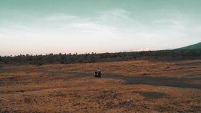 Silhouette travel people on motorbike riding through the lava-covered desert against the backdrop one of the most recognizable sights of Bali, the largest volcano Agung. 4K Aerial UHD Video Clip