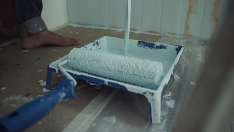 A stream of paint pours into the tray. A bath for painting with a roller. Roller with blue paint. Renovation of the room. Modern interior in the house. Self-isolation. Quarantine. Close up