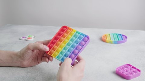 man playing pop it fidget toys, closeup on hands. unrecognizable male sits at table, pushes bubbles on colorful silicone poppit with fingers. close up on multicolor anti-stress toys. stress reliever