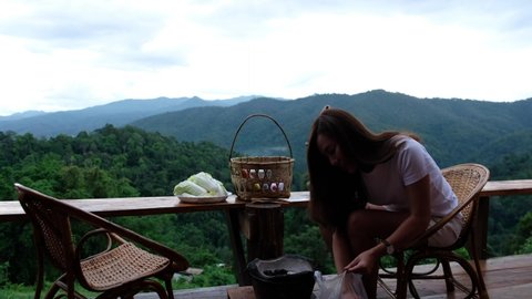 A woman preparing and putting charcoal into a stove before cooking Moo Kata, Thai barbecue grill pork on balcony with beautiful nature view