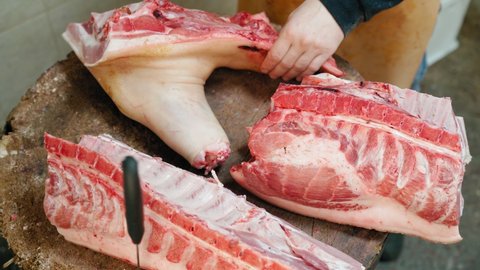 a professional person in the meat industry Cuts pieces of meat with a large butcher's axe. a man with a sharp knife cuts the carcass of a pig, separating the pieces of meat.