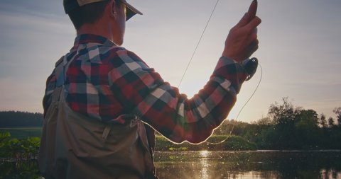 Fly fishing. Angler stands in the river and casts the fly at sunset with splashes. Fisherman fishing on fly on the calm river at sunset and casting the line with the Roll Cast