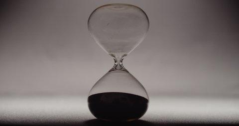 A hand rotating an hourglass with black sand to its cycle beginning.