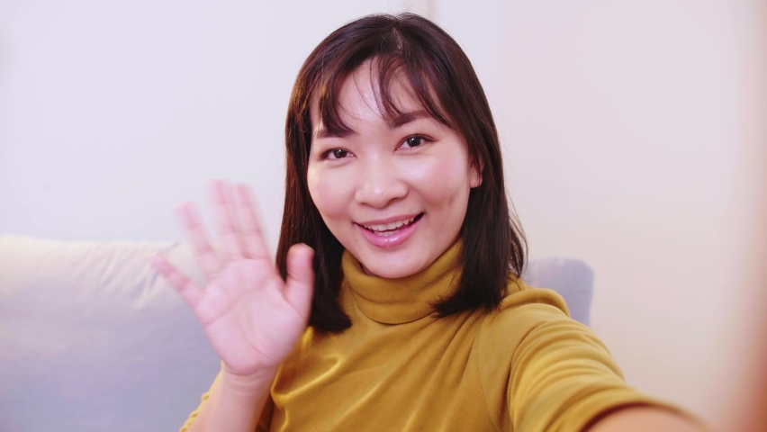 Lovely Asian woman making video call with family while preparing suitcases for clothes for travel.
