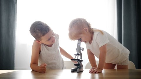 Child baby caucasian little boy scientist biologist researcher working with microscope and show it to his sister. Children Studying. science educaton concept. Biological laboratory