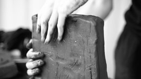 Close-up of female hands working with clay. Potter in the process of sculpting. Shaping a clay product. Black and white video. Pottery workshop. The artist sculpts from a dark plastic mass.