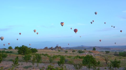 Goreme, Cappadocia, Turkey - May 27, 2021: Ballooning in Kapadokya. Many hot air balloons flying over spectacular breathtaking unusual valleys and rocks in blue sunrise morning sky. View from balloon