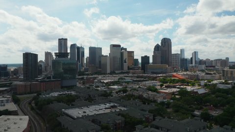 Panoramic aerial view of downtown skyscrapers behind rush highway. Forwards fly above low buildings. View against bright clouds in sky. Dallas, Texas, US in 2021