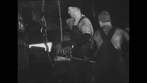 1940s: Man stands in front of furnace in foundry then moves as three men shove rod into furnace then remove rod along with molten hot metal shard.